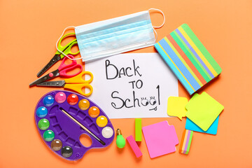 Naklejka na ściany i meble Paper with text BACK TO SCHOOL, stationery and medical mask on color background