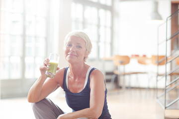 Older woman drinking juice on exercise mat