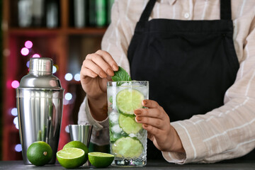 Female bartender making fresh mojito on table in bar