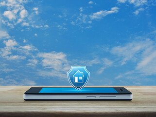 House with shield flat icon on modern smart mobile phone screen on wooden table over blue sky with white clouds, Business home insurance and security online concept