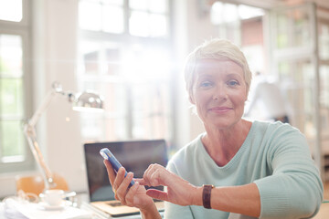 Businesswoman using cell phone at home office desk