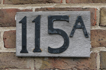Old weathered number 115a in black on wooden plaque attached to wall
