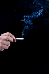 Black background. the hand of a man with roughened skin holds a cigarette. blue smoke is coming from it. close-up.