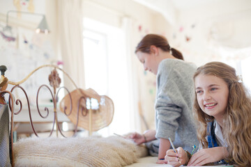 Two teenage girls on bed writing in notepads