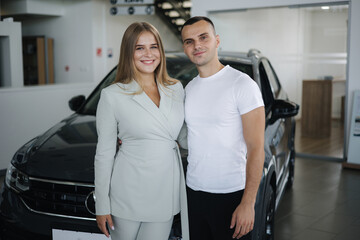 Portrait of beautiful young couple happy after buying new car from car showroom. Woman hus her man and glad