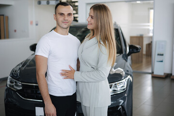 Portrait of beautiful young couple happy after buying new car from car showroom. Woman hus her man and glad