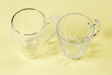 Two different empty glass cups on a yellow surface