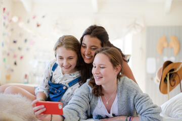 Obraz premium Three teenage girls using smart phone together while lying on bed