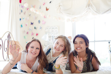 Three teenage girls lying on bed waving