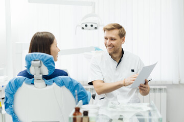 Male Professional Dentist With Gloves And Mask Holding papers photo And Show What The Treatment Will Look Like Of The Patient's Teeth. Discussion Of The Treatment Plan And Healthy Smile