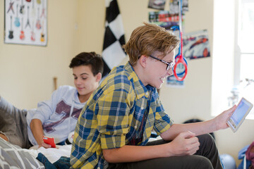 Two teenage boys using electronic devices in room