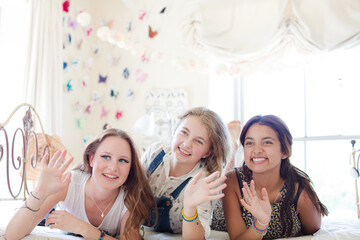Three teenage girls lying on bed waving
