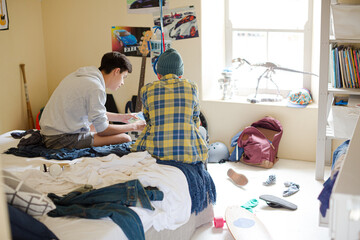 Two teenage boys sitting on bed in messy room