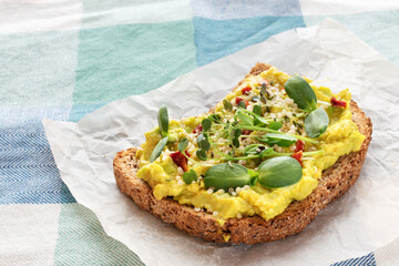 Raw toast with avocado, microgreens and hemp seeds on baking paper and tablecloth.