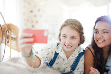 Three teenage girls taking selfie on bed in bedroom