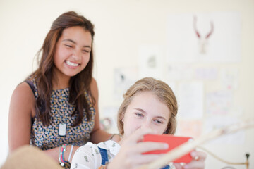 Two teenage girls sharing smart phone and smiling
