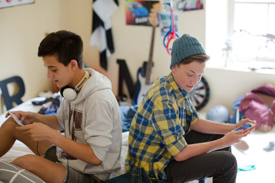 Two Teenage Boys Using Electronic Devices In Room