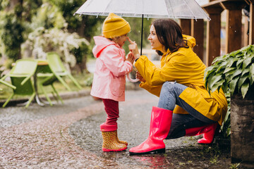 Mother with daughter walking in park in the rain wearing rubber boots