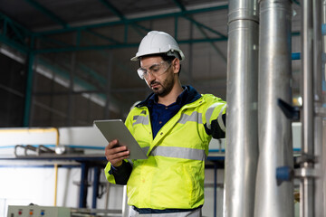 Male factory mechanic wearing safety glasses, white helmet. Technicians male working with digital tablet, checking the operation of equipment, repairing and maintenance machinery in industry factory