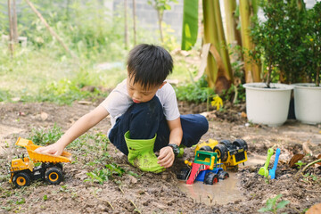 Cute Asian young schoolboy wearing rain boots playing in muddy puddles alone, Children getting...