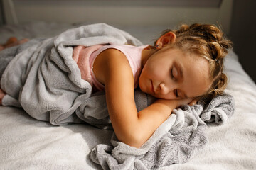Obraz premium Pretty little girl in pink pajamas sleeping in her bad at daytime. Healthy lifestyle concept.