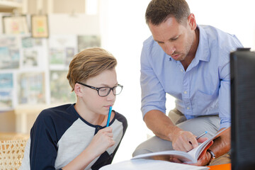 Father helping teenage son doing his homework in room
