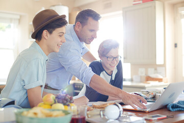 Teenage boys with father using laptop in dining room