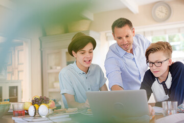 Teenage boys with father using laptop in dining room