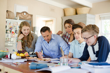 Teenagers with mid adult man sitting at table in dining room