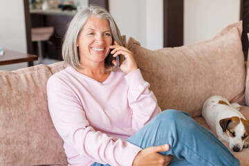 Pleased middle-aged white woman talking on mobile phone on couch