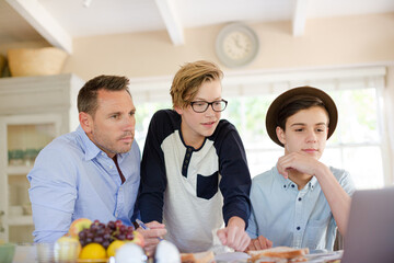 Teenage boys with father using laptop in dining room
