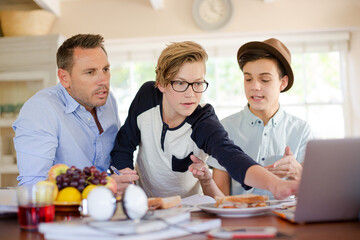Teenage boys with father using laptop in dining room
