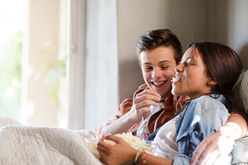 Teenage couple lying in bed and eating popcorn