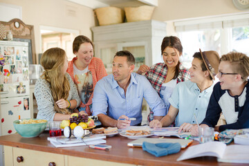 Teenagers with mid adult man sitting at table in dining room