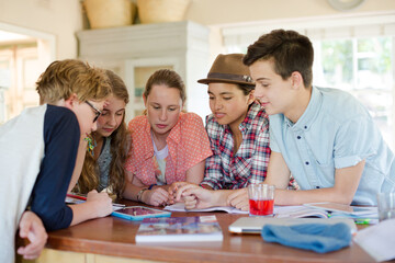 Group of teenagers using together digital tablet at table in kitchen