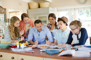 Teenagers with mid adult man sitting at table in dining room