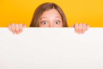 Portrait of school person eyes peeking behind large empty space wall isolated on yellow color...