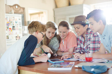 Group of teenagers using together digital tablet at table in kitchen