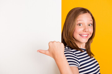 Photo of positive pupil indicate thumb empty space promotion toothy smile isolated on yellow color background