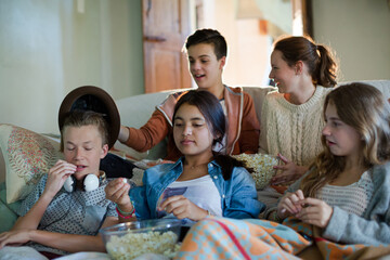 Group of teenagers throwing popcorn on themselves while sitting on sofa