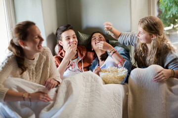 Group of teenagers throwing popcorn on themselves on sofa