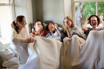 Group of teenagers throwing popcorn on themselves on sofa