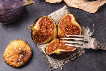 Ripe figs cut into three parts and dried fruit on sackcloth with a silver fork on a granite table. Fresh wholesome fruits of the new crop and dried fruits in the store for long-term storage