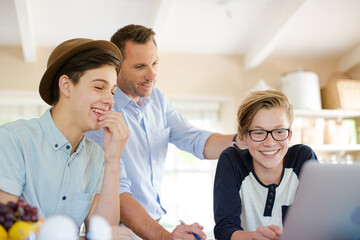Obraz premium Teenage boys with father using laptop in dining room