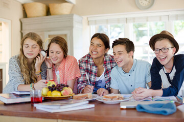 Group of smiling teenagers gathered around table in dining room