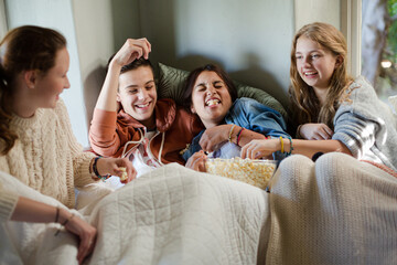 Group of teenagers throwing popcorn on themselves on sofa