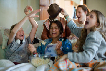 Group of teenagers throwing popcorn on themselves while sitting on sofa