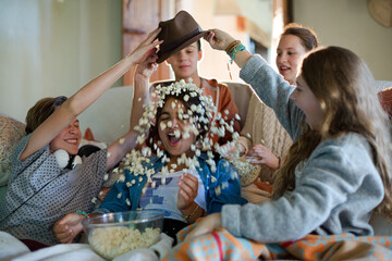 Group of teenagers throwing popcorn on themselves while sitting on sofa