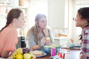 Teenage girls learning at table in kitchen