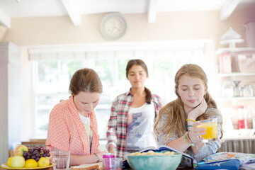 Teenage girls learning at table in kitchen